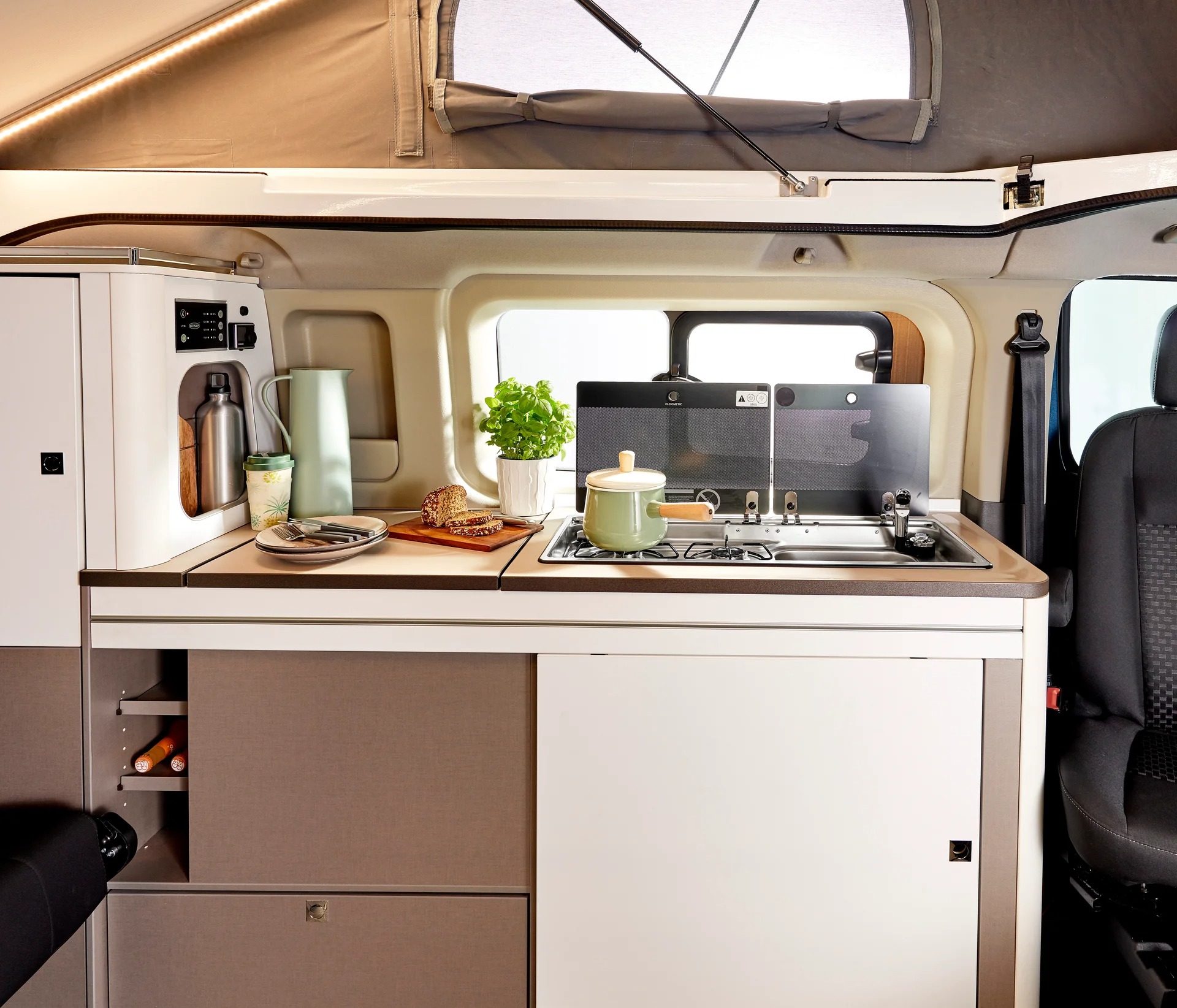 Litet kök i en kompakt husbil. Taket är upplyft och man ser tältduk med ett fönster som täcker.