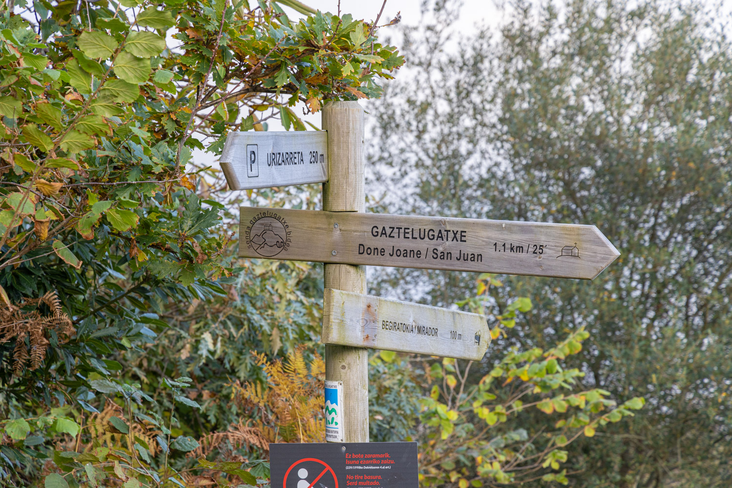 Skylt i trä som visar vägen till Gaztelugatxe (1,1 km), en utsiktsplats (100 meter) och parkering (250 meter).
