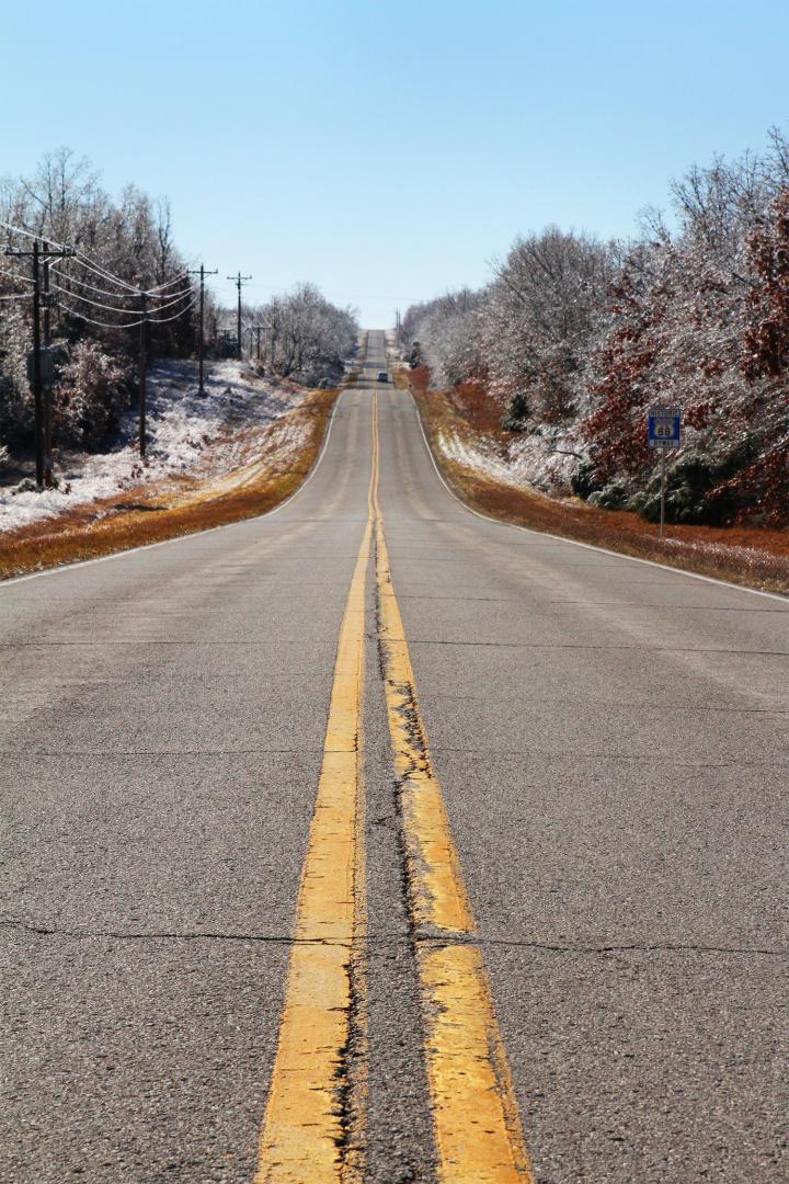 En typisk amerikansk landsväg med gula mittstreck. Vägen är omgärdad av skog med ett lätt snötäcke.