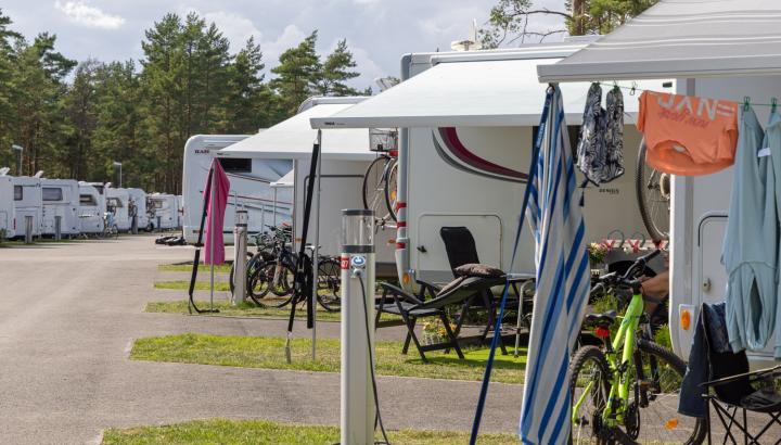 Camping med husbilar på rad ståendes på asfalt med gräsyta framför, där man ser campingmöbler, utdragna markiser, cyklar och kläder på tork.