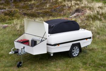 En vit camp-let-vagn med en öppen bagagebox med campingstolar och kylväska i, fastsatt på dragstången.