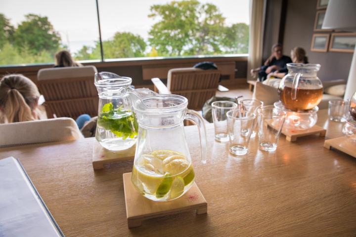I förgrunden syns ett bord med vattenkaraffer med citron och lime i en och myntablad i en annan. Glas står uppställda och här finns också en tekanna. I bakgrunden ser man ett stort fönster med vacker utsikt och framför det finns bekväma fåtöljer.