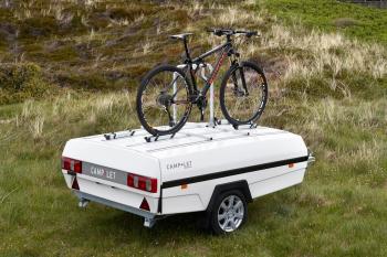 En vit camp-let-vagn med ett cykelställ och en mountainbike.